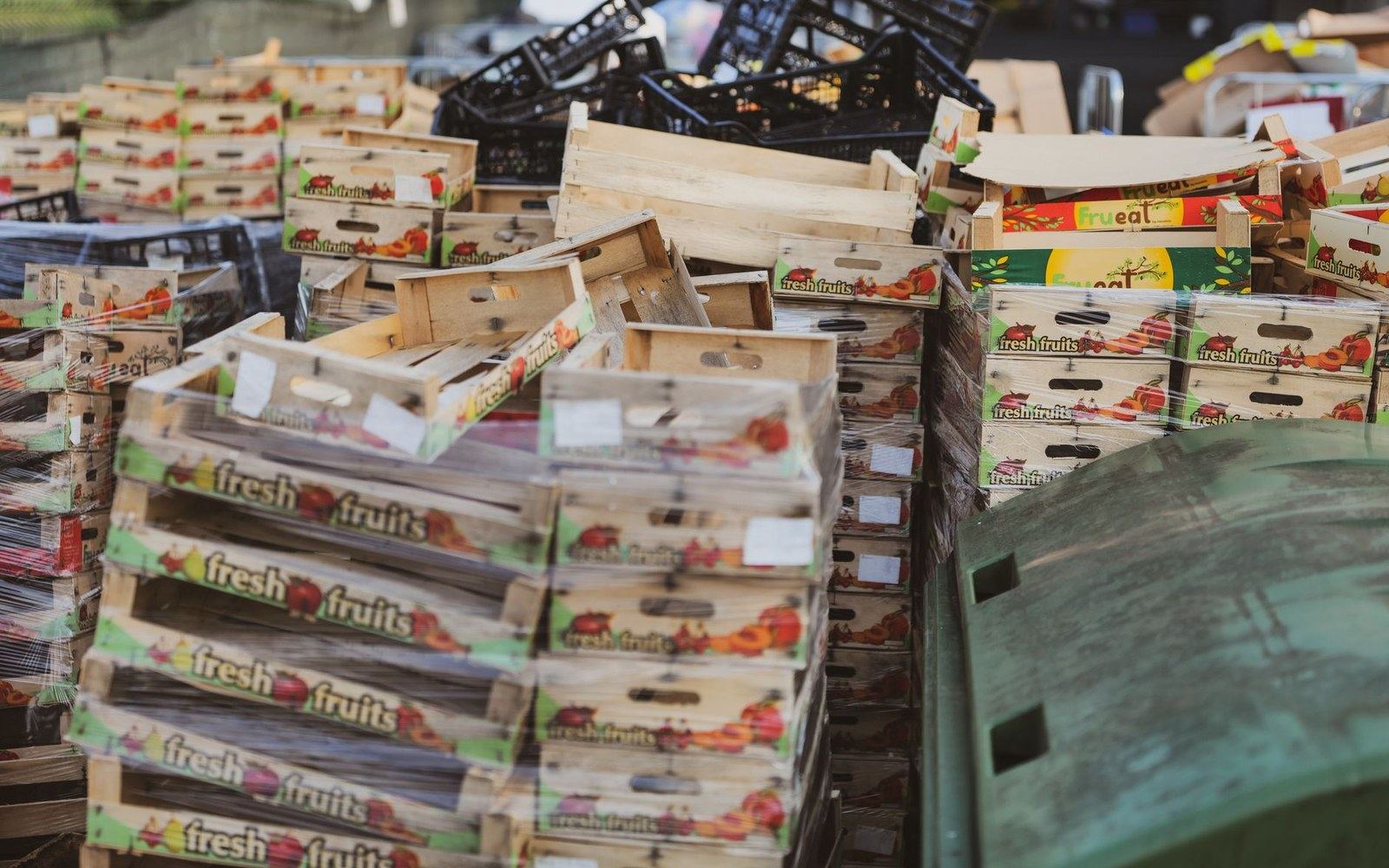 Stacks of empty wooden fresh fruit crates piled beside plastic bins outdoors