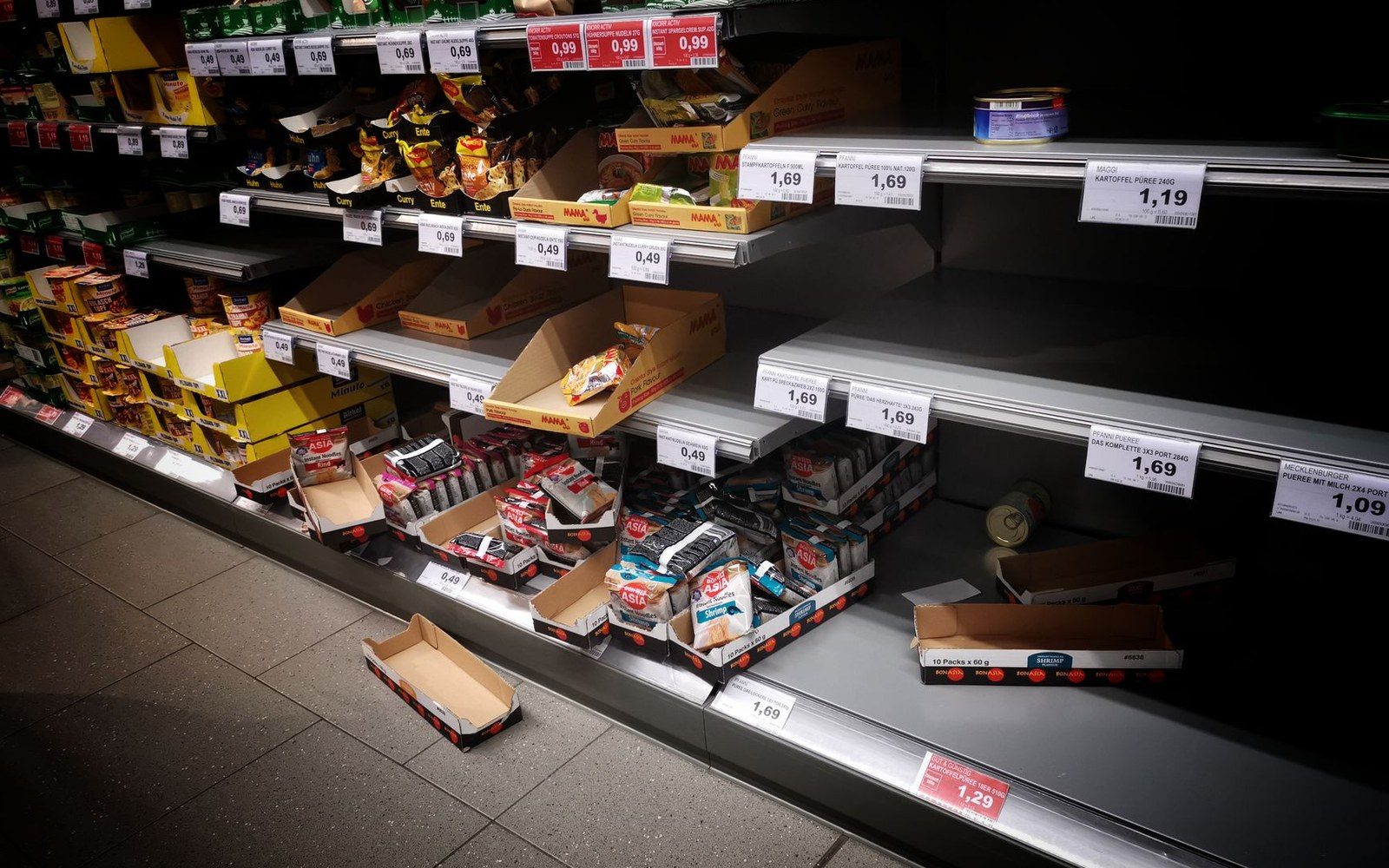 Nearly empty supermarket shelves with price tags and scattered cardboard boxes
