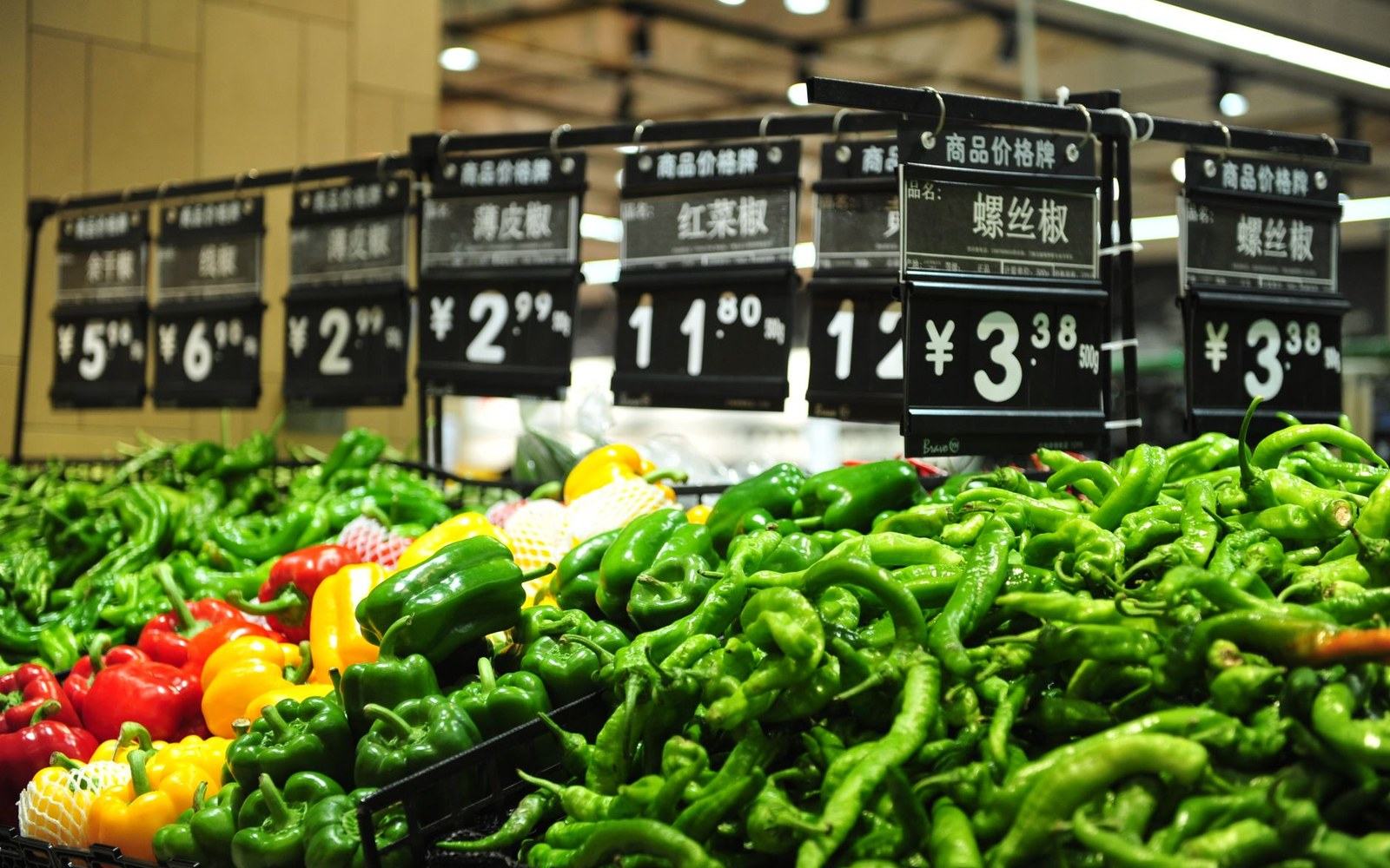 Fresh chili peppers and bell peppers displayed with Chinese yuan price signs at a supermarket