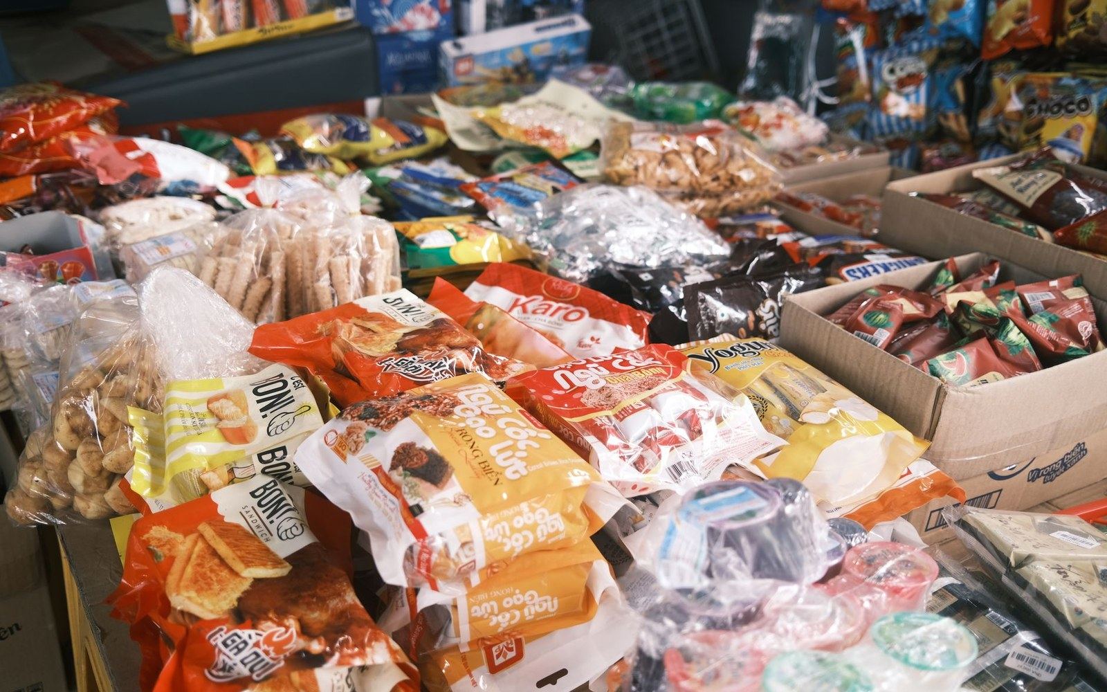 Packaged snacks and candies displayed in boxes on a market stall table